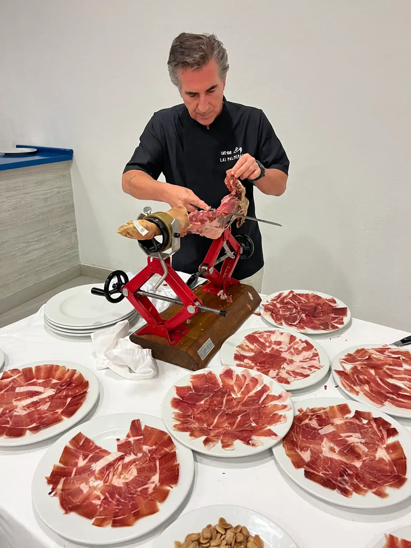 Sergio, cortador profesional, cortando jamón con el jamonero Carher94 rojo junto a una mesa llena de platos de jamón en un evento