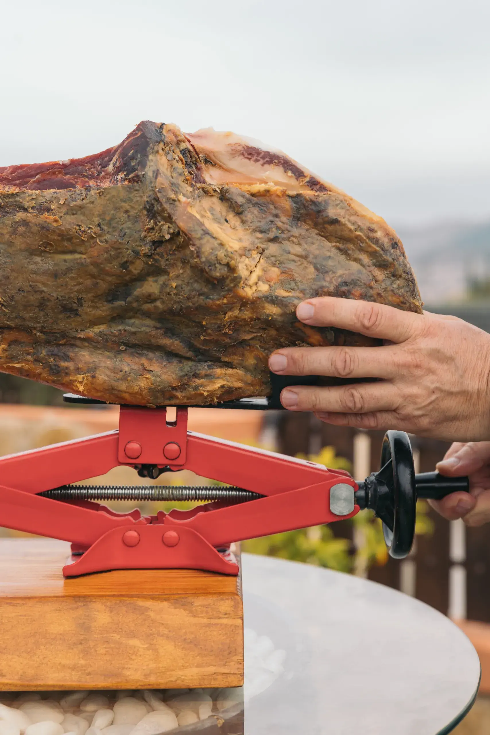 Una mano apoyada sobre la maza del jamón, que descansa en el soporte rojo